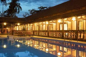 Área da piscina com o reflexo do interior do edifício, um banco e um corrimão.