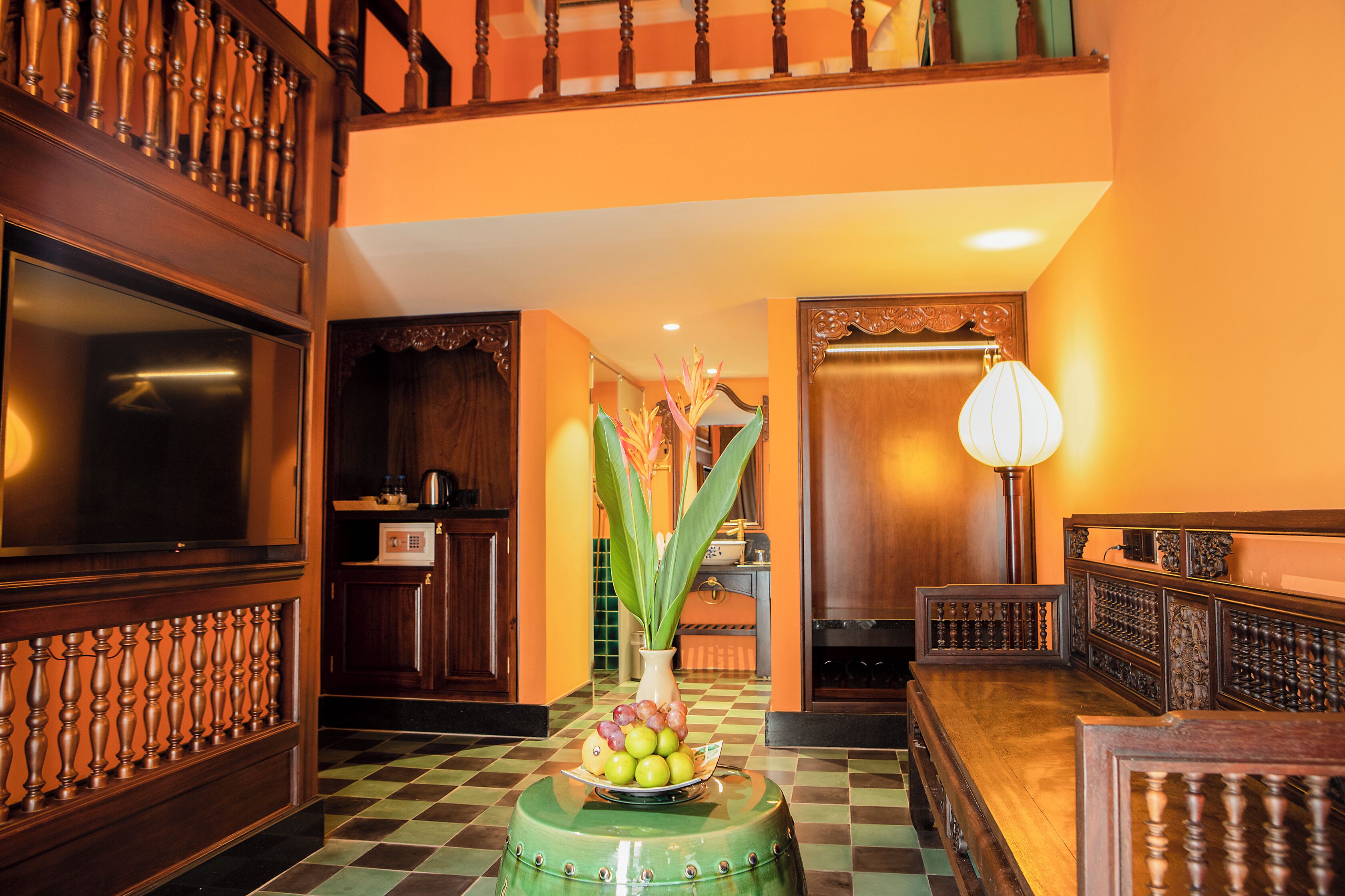 A hotel lobby with a checkered floor, a green round table with fruit, and a staircase with wooden balusters.