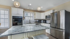 Una cocina moderna con armarios blancos, un refrigerador de acero inoxidable, encimera de mármol e iluminación colgante.