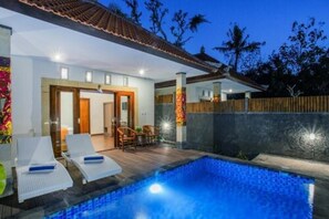 A swimming pool with lounge chairs, a wooden deck, and a covered patio area.