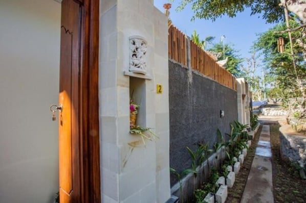 A narrow pathway flanked by a stone wall and a wooden fence, leading to a building entrance.