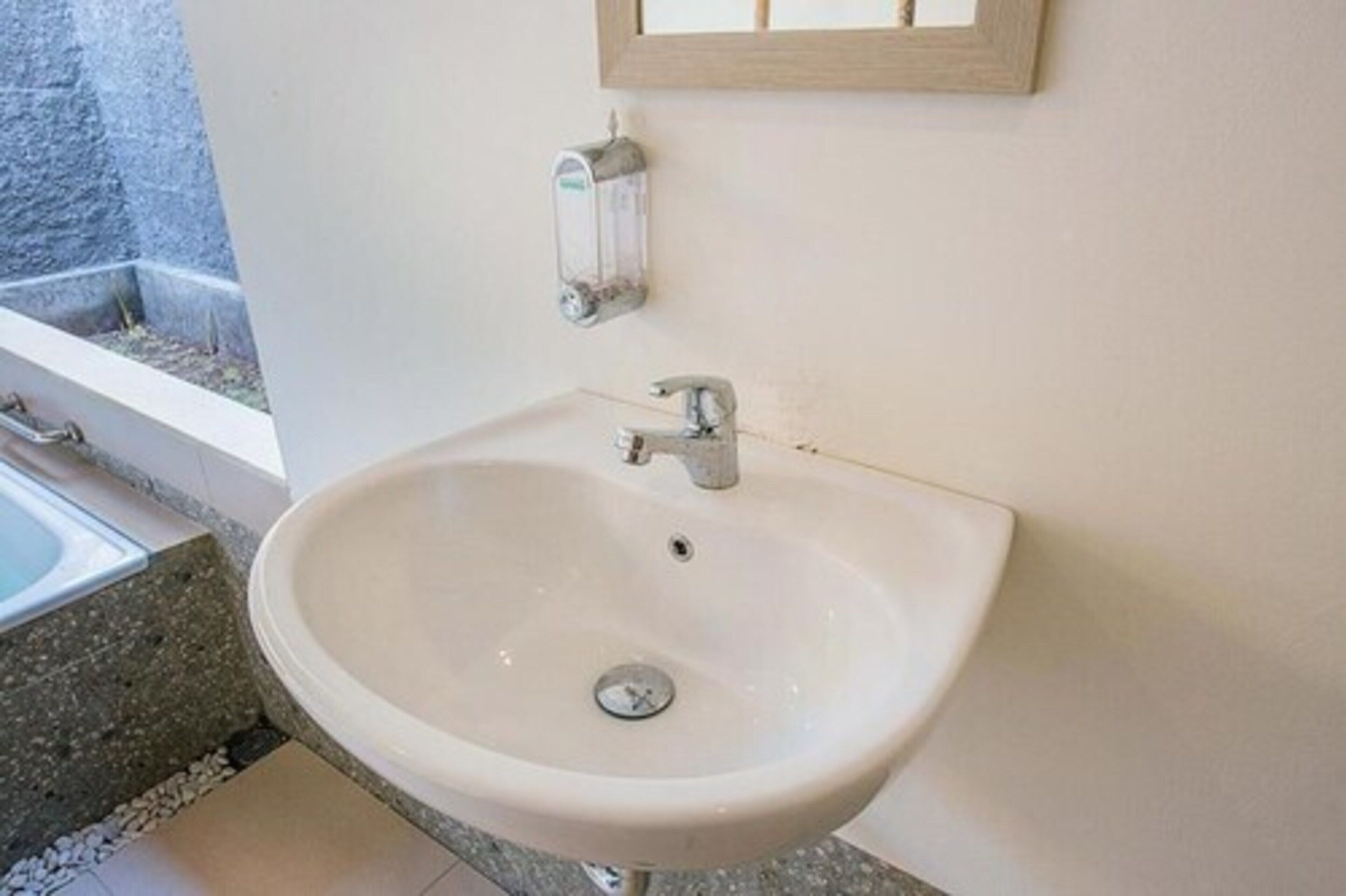 Une salle de bain avec un lavabo blanc, un robinet et un distributeur de savon fixé au mur.