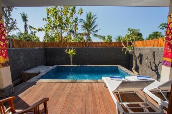 A pool area with wooden deck, lounge chairs, and a view of palm trees.