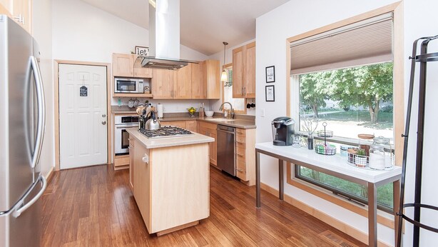 A modern kitchen with wooden cabinets, a central island, a built-in microwave, and a large window offering a view of the outdoors. - 2bed/2bath Large bright and comfortable home (Rochester)
