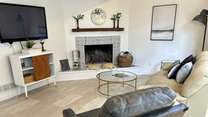 A modern living room with a leather sofa, a round coffee table, a white entertainment unit, a fireplace, and a mounted TV. - 2bed/2bath Large bright and comfortable home (Rochester)