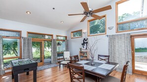 A dining area with a wooden table, chairs, and a foosball table. There are large windows with curtains, a ceiling fan, and a wall-mounted light fixture. - 2bed/2bath Large bright and comfortable home (Rochester)