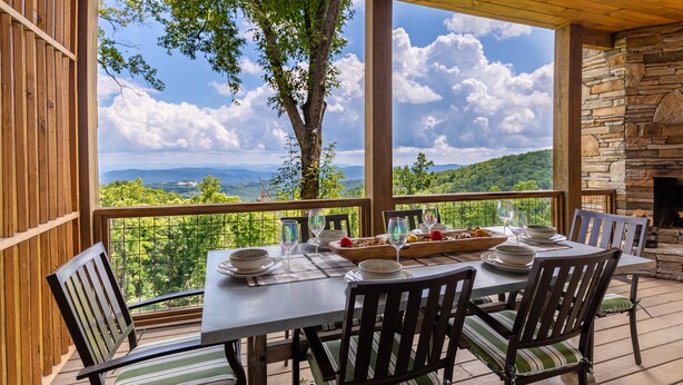 A wooden deck with a table set for dining, overlooking a mountainous landscape. - Blue Ridge Bliss - BRMC amenities, views, firepit, indoor and outdoor gas fireplace (Boone)