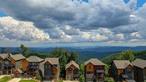 A row of modern, multi-story houses with large windows and balconies, set against a backdrop of rolling hills and a cloudy sky. - Blue Ridge Bliss - BRMC amenities, views, firepit, indoor and outdoor gas fireplace (Boone)