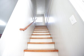 Eine Treppe mit Holzbeschlägen und Geländer, die zu einer Zwischenebene mit einem kleinen Fenster hinaufführt.