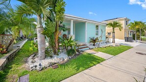 Una casa residencial con porche, rodeada de plantas tropicales y un césped bien cuidado.