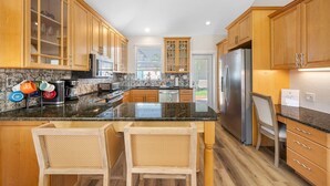 Una cocina moderna con armarios de madera, encimera de granito, electrodomésticos de acero inoxidable y una zona de estar con dos sillas.