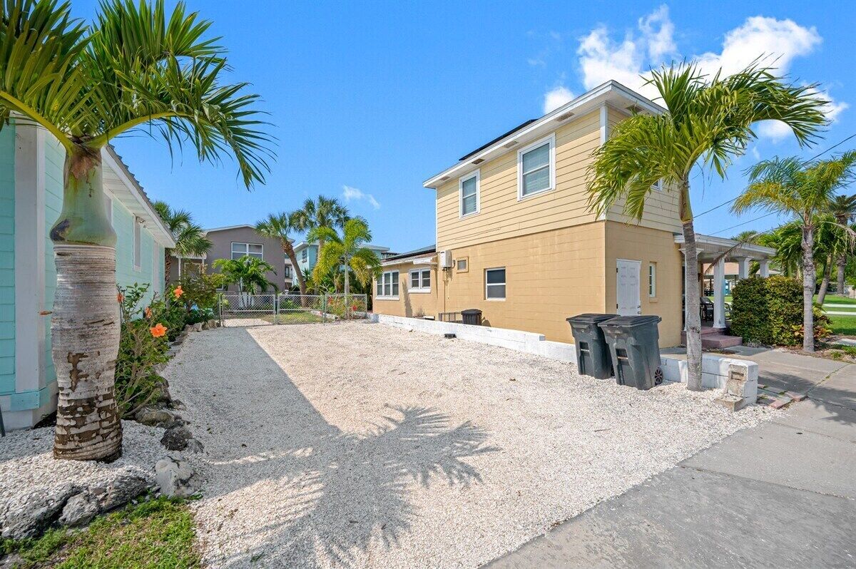 A residential area with houses, palm trees, and a gravel driveway.
