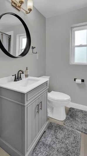 A bathroom with a white sink, a mirror, a toilet, and a window.
