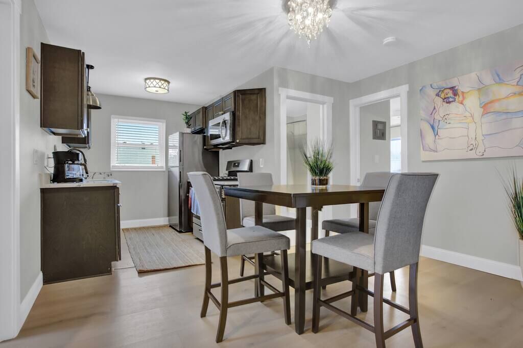 A modern kitchen with dark cabinetry, a dining table with four chairs, and a chandelier.