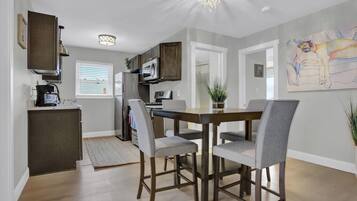 A modern kitchen with dark cabinetry, a dining table with four chairs, and a chandelier.