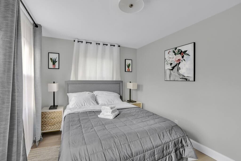 A modern bedroom with a large bed, two bedside tables with lamps, a headboard, and two framed artworks on the walls.