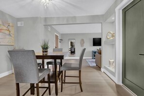 A dining area with a wooden table and chairs, a chandelier, and a television on a shelf.
