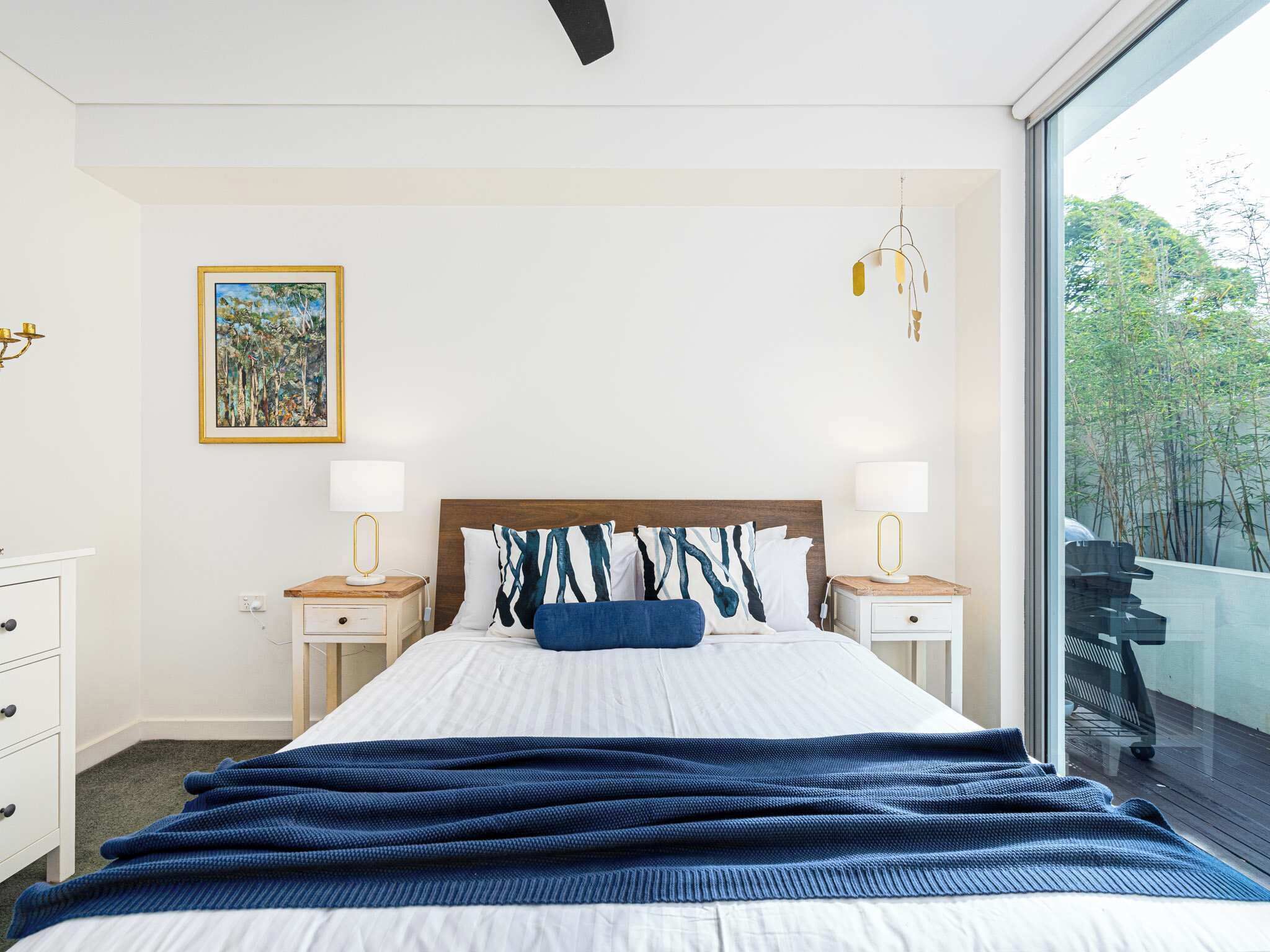 Une chambre à coucher avec un lit, deux tables de chevet, une commode, une fenêtre donnant sur un beau paysage et un tableau accroché au mur.
