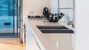 A modern kitchen with a gas stove, a coffee maker, and a unique black geometric sink. - The Garden Retreat (Bondi Junction)