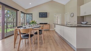 A modern kitchen with a dining area, large windows, and a flat-screen TV. - Luxury Waterfront Retreat on Murray River (Moama)