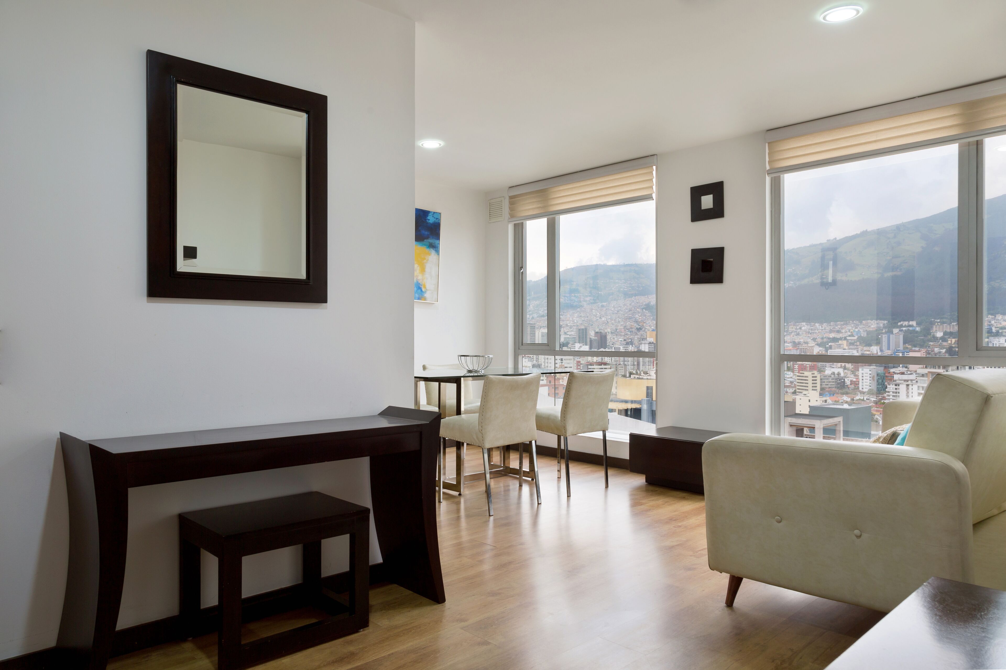 A modern living room with a large window, a dining area, and a view of a cityscape.