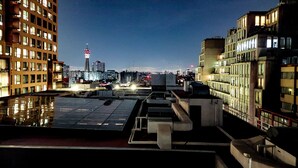 Terraza en la azotea con vistas al horizonte urbano nocturno, que incluye edificios modernos y una torre con señalización iluminada.