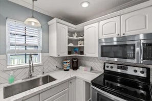 A modern kitchen with white cabinets, a stainless steel oven, a microwave, and a sink with a faucet.