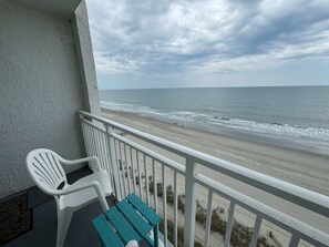 Un balcón con vista a la playa, una silla blanca y un banco azul turquesa.