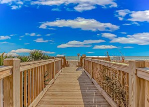 Un paseo marítimo de madera que lleva a una playa bajo un cielo despejado.