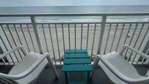A balcony with a view of the beach, white plastic chairs, and a small table. - Sea Mist 20909 (Myrtle Beach)
