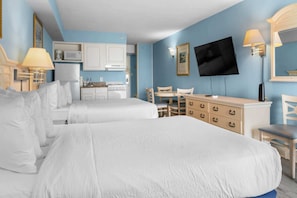 Ein Hotelzimmer mit zwei Betten, einer Küchenzeile, einem Fernseher und einem Schreibtisch mit Stühlen.