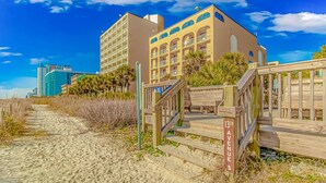 A beachfront hotel with a wooden boardwalk leading to the entrance, a clear blue sky, and a building with multiple balconies. - Sea Mist 20909 (Myrtle Beach)