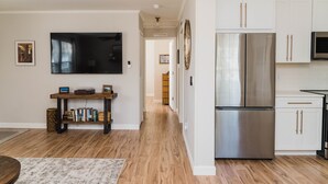 A modern kitchen with white cabinets, a stainless steel refrigerator, and a flat-screen TV mounted above the counter. - Beautiful Cottage-Style Home Minutes From Downtown Charleston! (Charleston)