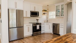 A modern kitchen with white cabinetry, stainless steel appliances, and a wooden dining table. - Beautiful Cottage-Style Home Minutes From Downtown Charleston! (Charleston)
