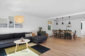 A modern living room with a sofa, a dining table with chairs, and a kitchen area.