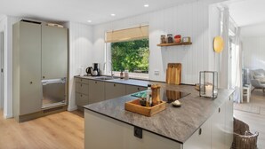 A modern kitchen with a central island, built-in appliances, and a view of greenery outside.