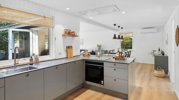 A modern kitchen with a built-in oven, a large window, and a dining area with a table and chairs.