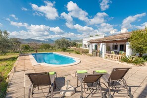 A swimming pool with lounge chairs, a patio, and a view of mountains.