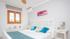 A bedroom with a bed, white nightstands, a window, and an air conditioning unit.