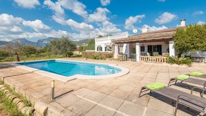 A poolside area with a swimming pool, lounge chairs, and a building with a tiled roof.