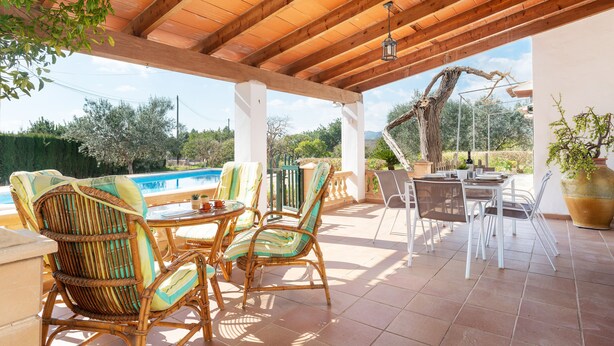 A covered outdoor patio with wicker furniture, a pool, and a view of the surrounding landscape.