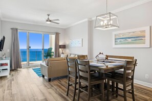 Zona pranzo con tavolo e sedie, ventilatore a soffitto e vista sull'oceano attraverso ampie finestre.