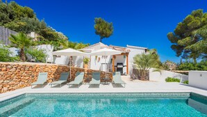 A poolside area with a stone wall, lounge chairs, and umbrellas. - CostaBlancaDreams - Villa Nathalie in Moraira (Moraira)