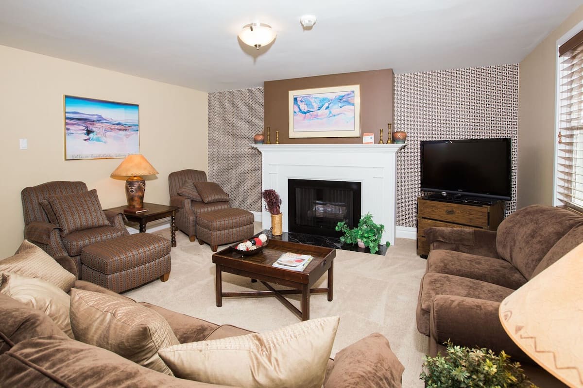 A living room with a fireplace, a television, and patterned wallpaper.