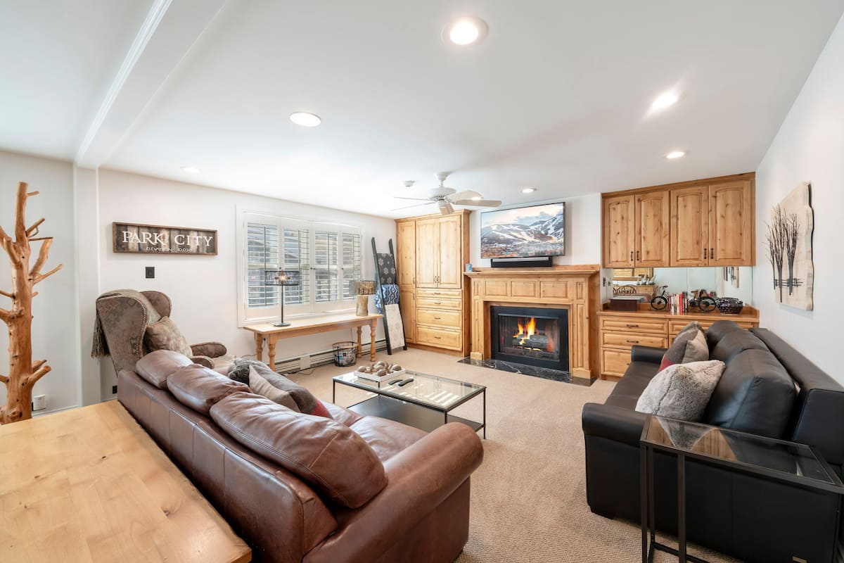 A modern living room with a fireplace, leather sofas, a television, and wooden cabinets.