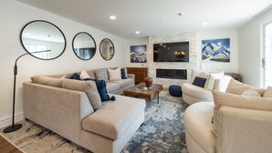 A modern living room with a beige sofa set, a coffee table, and a fireplace. There are three round mirrors on the wall and a large painting above the fireplace. - Resort Plaza Condominiums 5030 - 5064 (Park City)