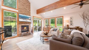 A spacious living room with a fireplace, large windows, and a ceiling fan.