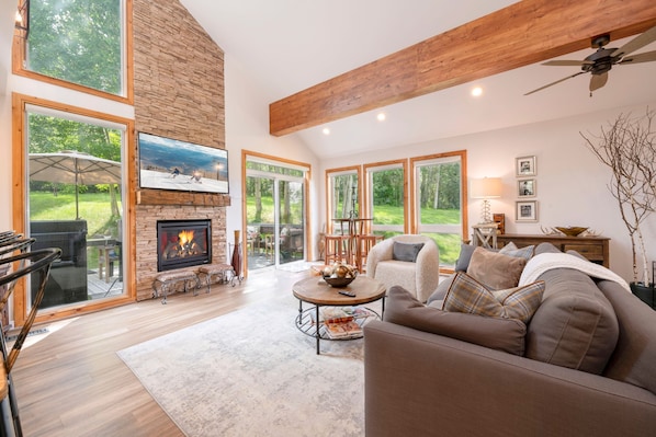 A spacious living room with a fireplace, large windows, and a ceiling fan.