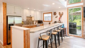 A modern kitchen with white cabinets, a stainless steel refrigerator, a large island with bar stools, and a stone backsplash.