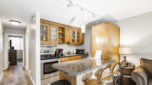 A modern kitchen with granite countertops, stainless steel appliances, wooden cabinets, and a bar area with stools.